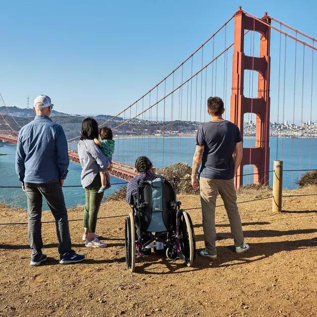 一群人, 包括一个坐轮椅的人, é visto por trás enquanto olham para a 金门大桥 de Marin Headlands.